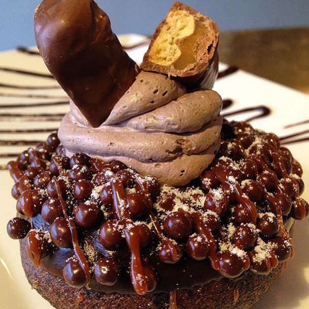 = Donut Crush Wednesday!! 😍🍩🍫👉🏽 Chocolate donut dipped in warm chocolate & chocolate crisp pearls topped with whipped chocolate mousse. Ending off with a bar on top & powered sugar!!